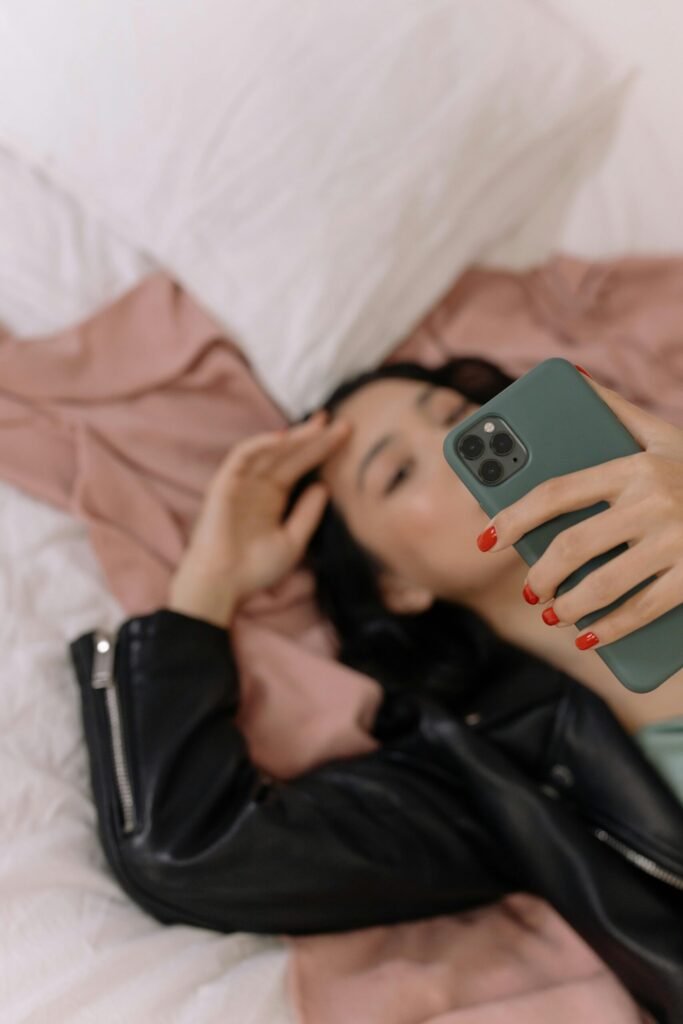 pexels-photo-6965103-6965103 A woman lying on a bed taking a selfie with her smartphone, wearing a leather jacket.